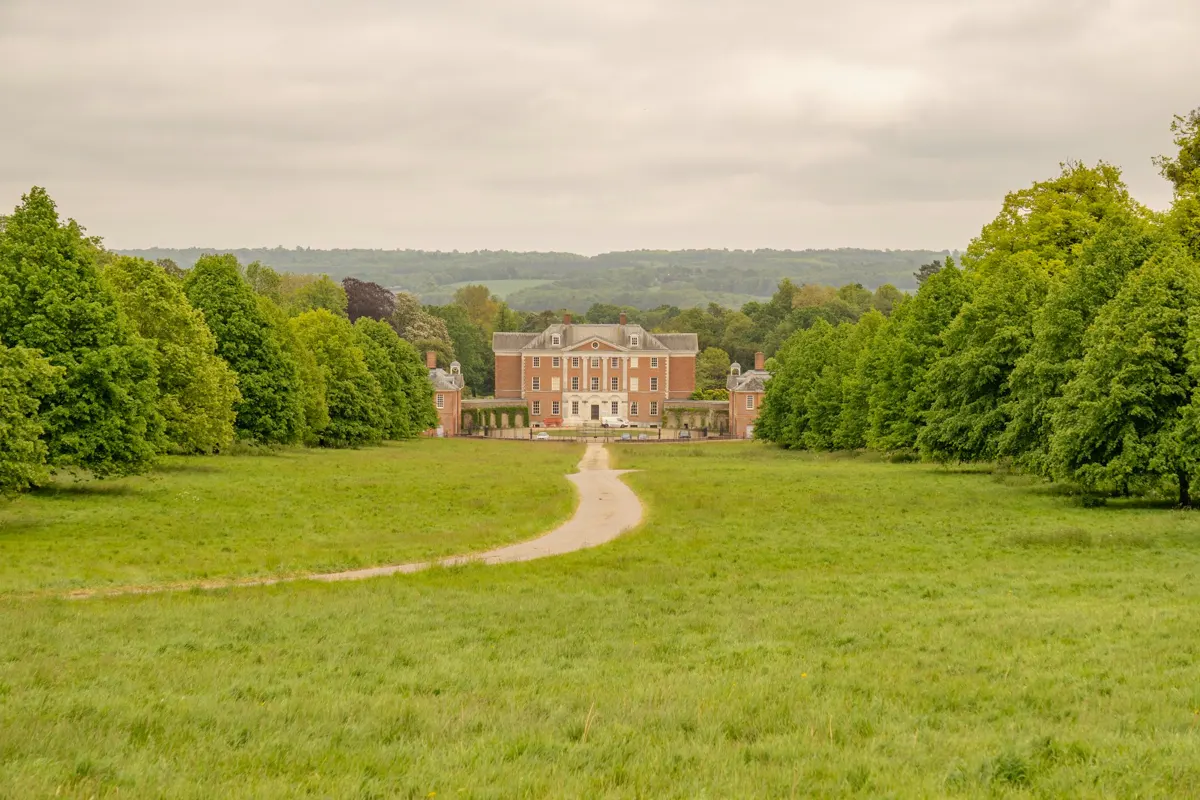 A red-brick country manor surrounded by trees and a long approach